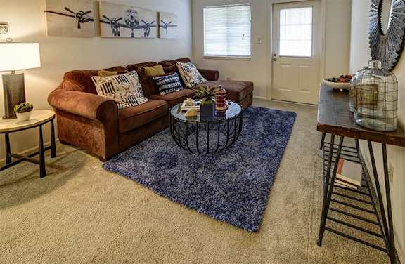 A living room with a brown couch, a blue rug, and a painting on the wall.