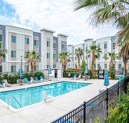 A swimming pool surrounded by palm trees and lounge chairs in front of a building.