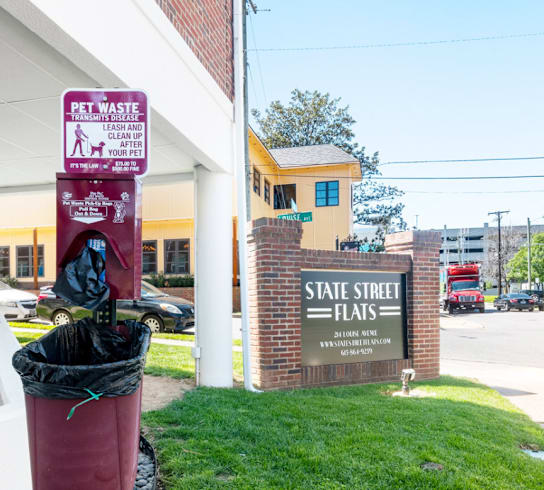 A sign on a pole that says "Pet Waste" and "Clean Up Your Pet's Waste".