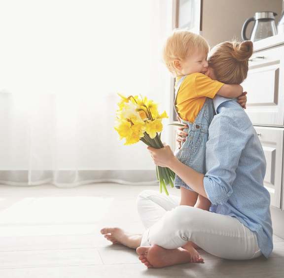 a woman sitting on the floor holding a baby and a bouquet of flowers