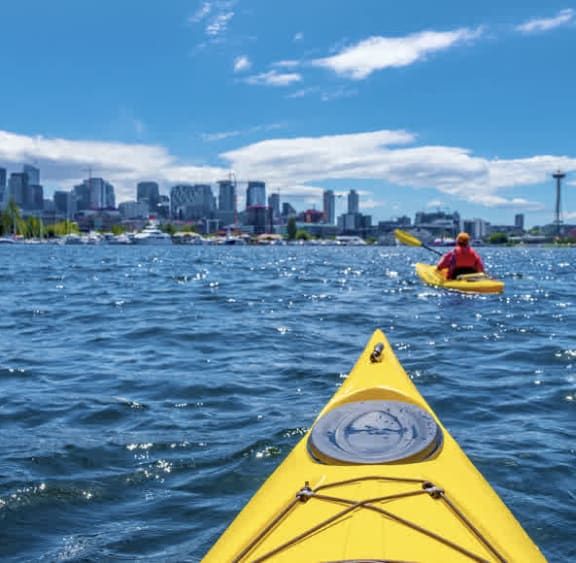 a man in a yellow kayak on the water with a city skyline in the