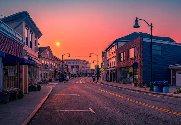 A street view of a town with buildings on both sides and a sunset in the background.
