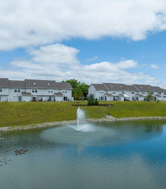 A fountain in the middle of a pond in front of a row of houses.