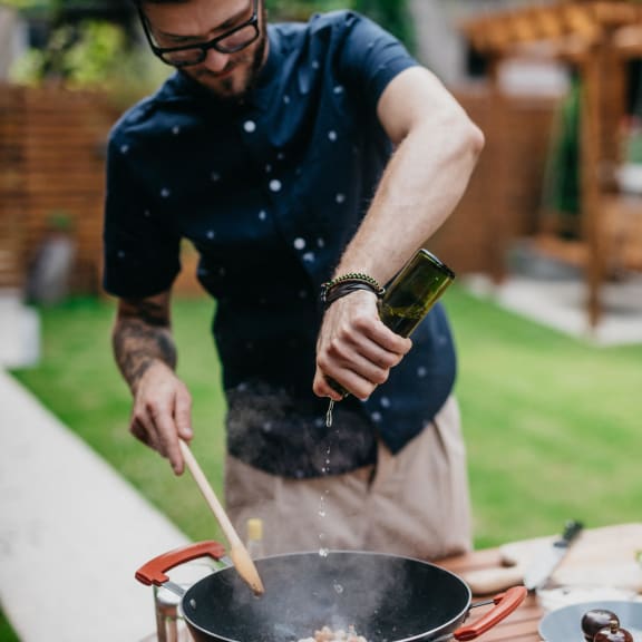 a man pouring wine into a pan of food on a table at Stone Creek at Old Farm Apartments, Houston, TX 77063