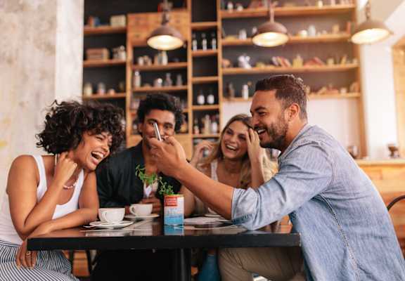 A man is playfully pointing at a woman while sitting at a table with two other people.