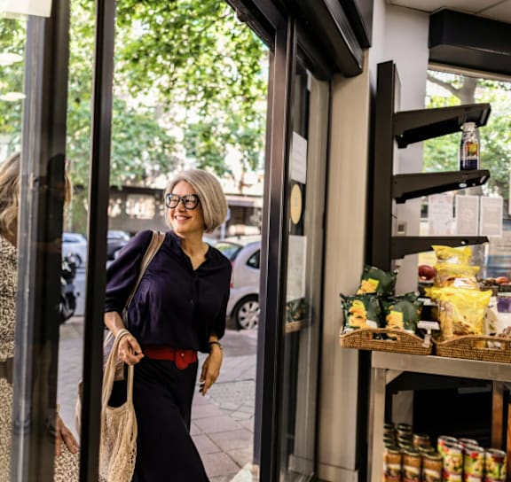 A woman in a purple shirt and black pants is entering a store.