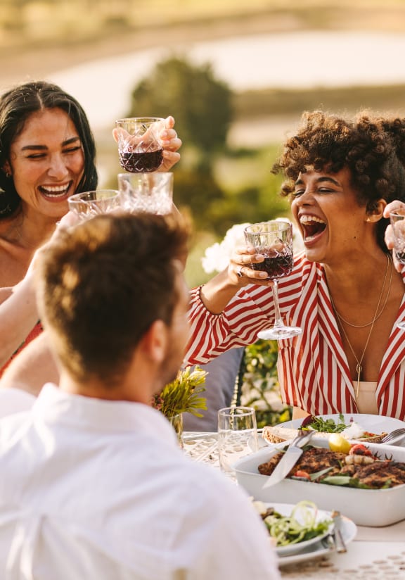 a group of people sitting around a table eating and drinking wine