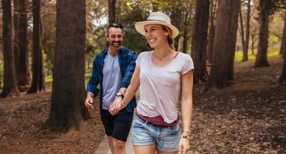 A man and a woman are walking hand in hand in a forest.