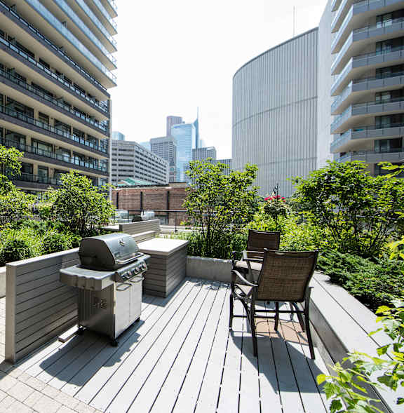A rooftop patio with a grill and chairs overlooking a city skyline.