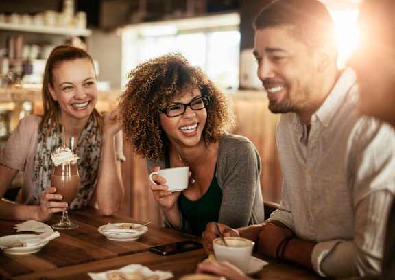 Three people are sitting at a table with drinks and food.