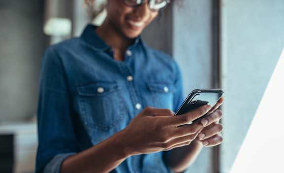 A person in a denim shirt is holding a smartphone.