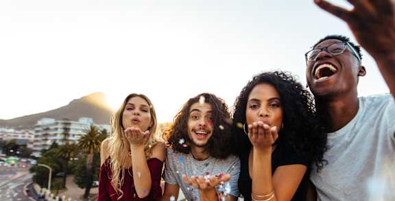 Four friends are taking a selfie on a balcony with a cityscape in the background.