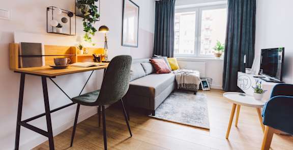 A chair with a teal cushion is in the center of a room with a table and a cactus.