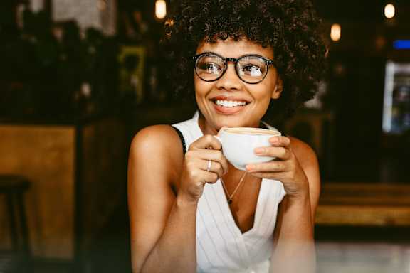 A woman with glasses is holding a cup and smiling.