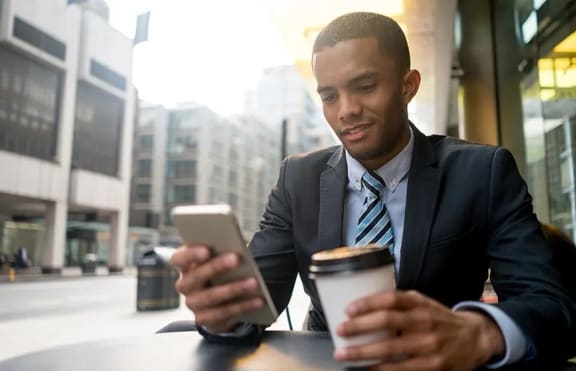 a man in a suit and tie holding a cup of coffee and looking at his phone