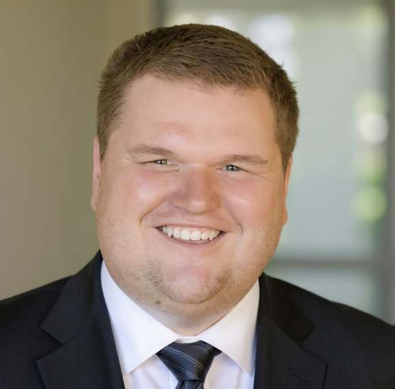 A man in a suit and tie smiles at the camera.
