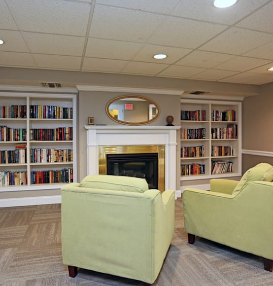 a library with two green chairs and a fireplace