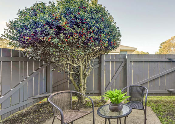 A tree with purple flowers is in the middle of a patio with two chairs and a table.