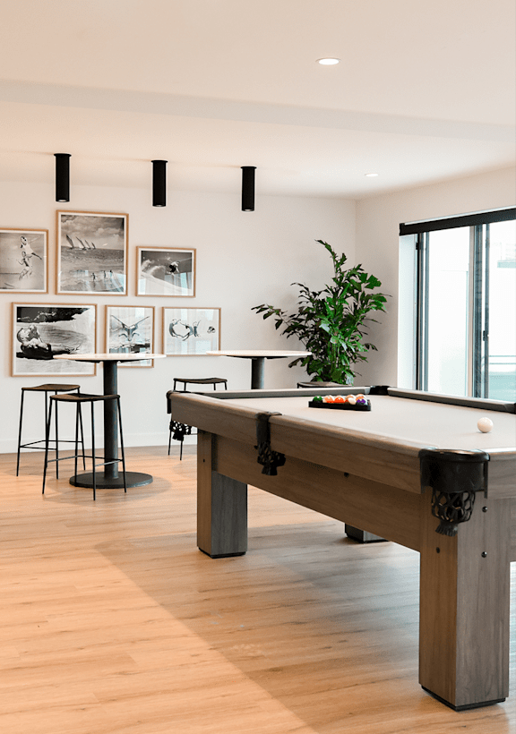 A pool table in a room with a plant and pictures on the wall.