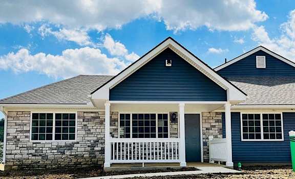 a blue house with a white porch and a blue sky with clouds