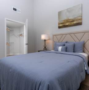 A bed with a blue comforter and two lamps on a side table.