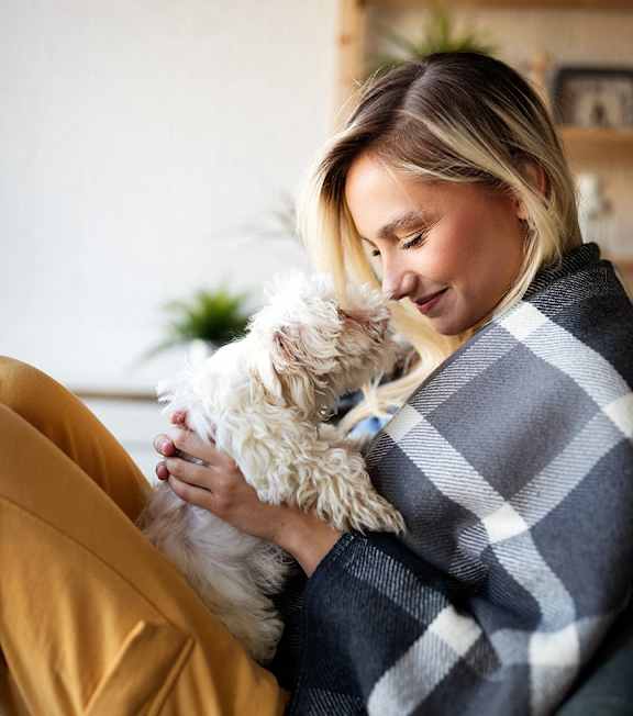 A woman is sitting on a couch holding a small white dog.