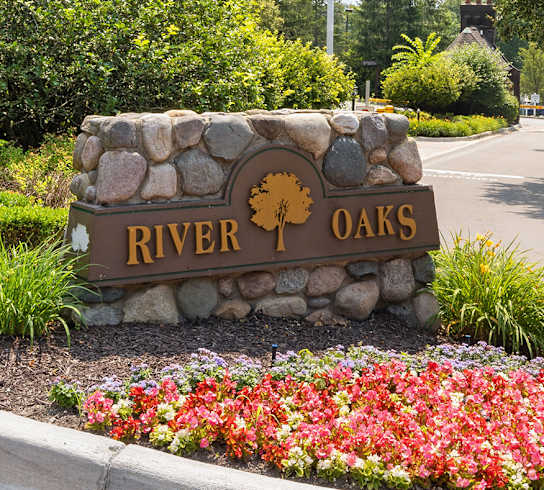 A sign that says River Oaks in front of a road.