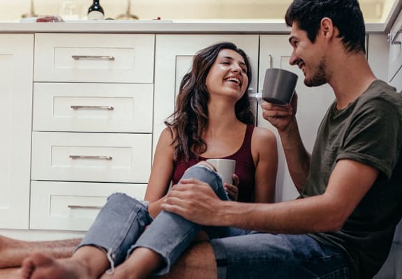 Couple sitting on kitchen floor with coffee l Las Casitas Apartments in Hisperia Ca 