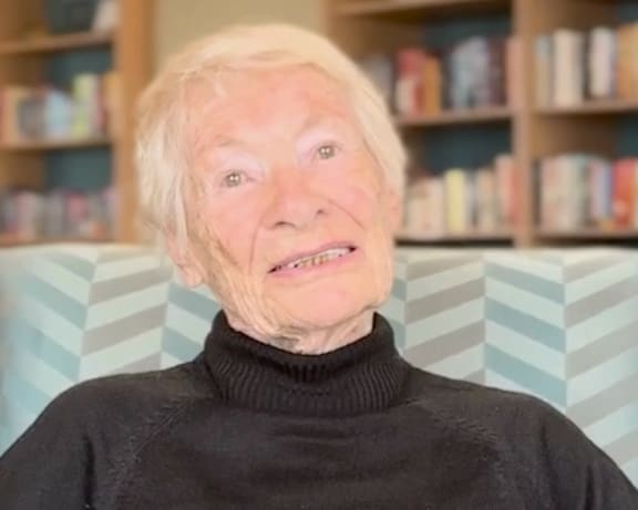 An elderly woman is reading a book on a couch.
