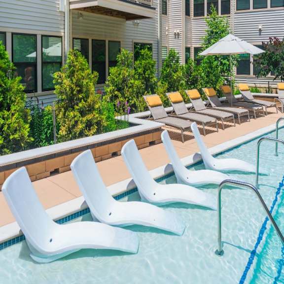 A pool with white chairs and a building in the background.