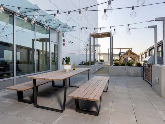 a patio with a wooden table and benches and a string of lightbulbs hanging above it