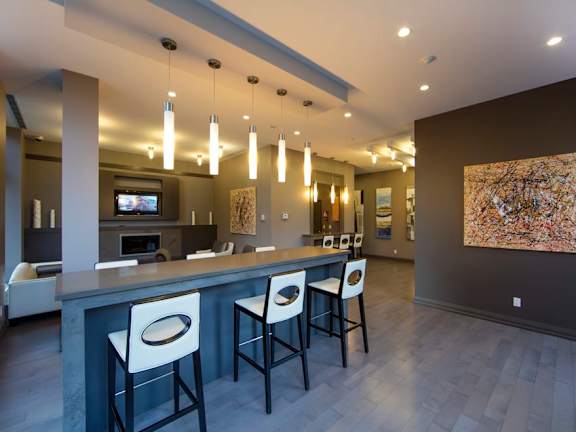 a bar with white chairs and a gray countertop in front of a living room with a