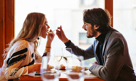 A man feeds his girlfriend a piece of food while they are sitting at a table.