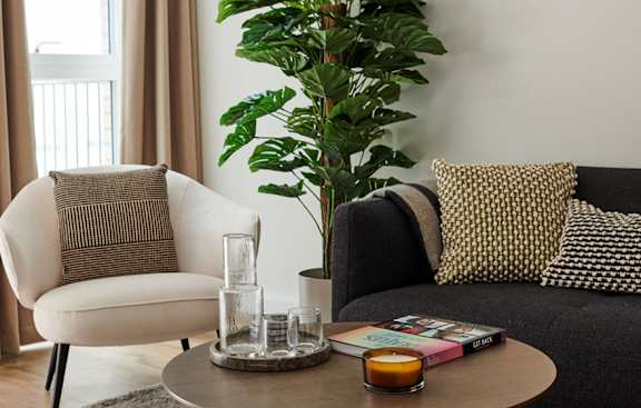 A living room with a black couch, a white chair, and a coffee table with a glass and a book on it.