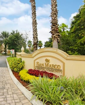 The image shows a beautiful entrance to San Marco Royal Country Club with a clear blue sky and lush greenery. at San Marco Apartments, Ormond Beach, FL, 32174