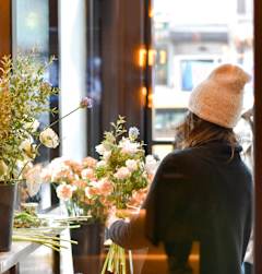 A woman in a white hat is looking at flowers in a vase.