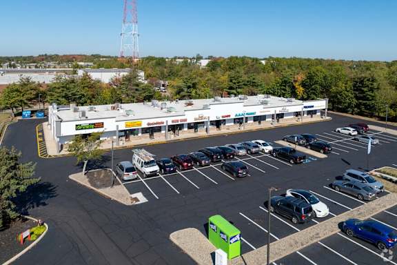 A parking lot with cars and a green trash can in front of a store.