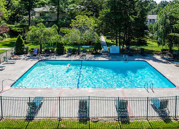A large swimming pool surrounded by a black fence and lounge chairs.
