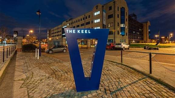 a sign for the keel on a city street at night at The Keel Apartments, Liverpool, L3 4GE