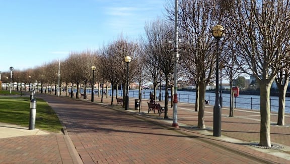 a sidewalk next to the water with benches and trees at Vox Apartments, Manchester