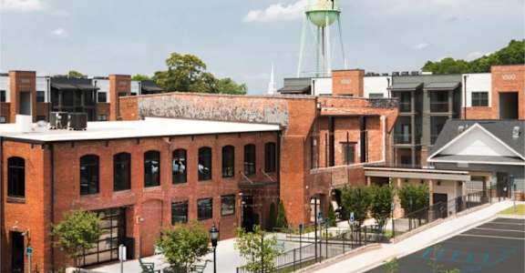A water tower with a bird on it is behind a building with a brick facade.