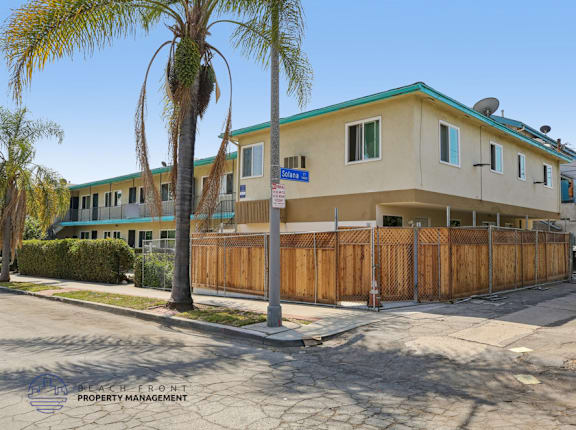 A building with a blue sign on the front is surrounded by a wooden fence.