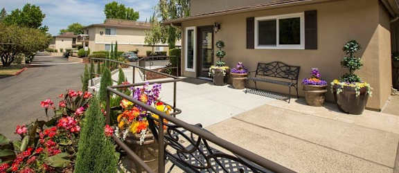 a patio with flowers and a bench in front of a house at Abby Creek Apartments, Carmichael California