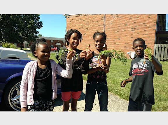 Four children holding plants in front of a brick building.