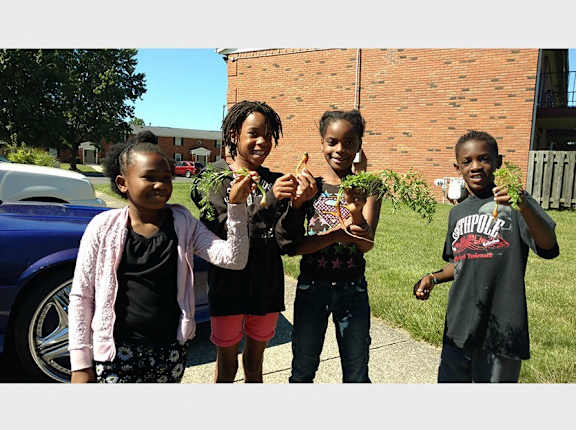 Four children holding plants in front of a brick building.