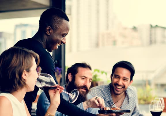 Group of people are sitting at a table in a restaurant eating and drinking wine