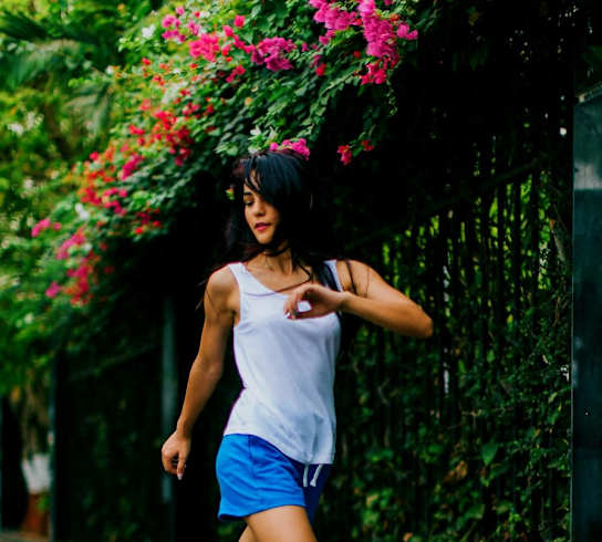 a woman in a white tank top and blue shorts running down a sidewalk