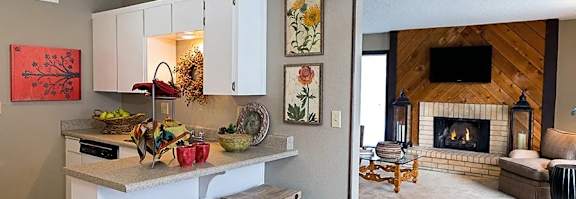 A kitchen with white cabinets and a breakfast bar beside a living room with a fireplace.