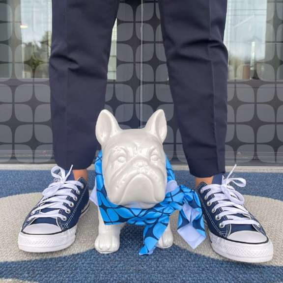 A person wearing dark pants and blue Converse shoes is standing next to a white bulldog figurine.