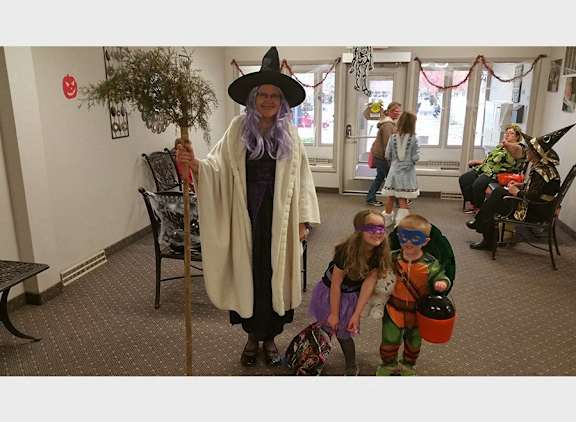 A person in a witch costume stands in a room with children.